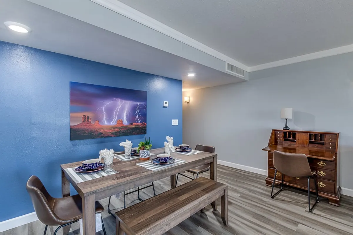 A contemporary dining area featuring a spacious table, modern wall art, and a desk, designed for shared meals, creative work sessions, or relaxed evening conversations among friends or neighbors.