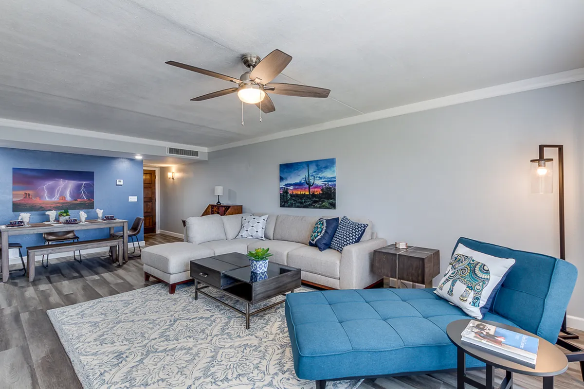 A stylish living area with a plush sectional sofa, a blue accent chair, a coffee table, and vibrant wall art. The overall ambiance is welcoming and comfortable, ideal for unwinding or socializing. Natural light enhances the inviting atmosphere, making the room feel like a true sanctuary.