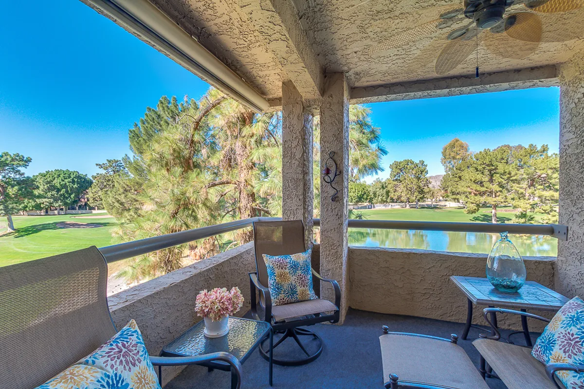 A beautifully arranged balcony seating area overlooking the lush Biltmore golf course, with cozy decorative pillows, a flower vase on the table, and ample space for relaxing or entertaining. The view extends to distant mountains, and the scene is bathed in warm sunset light.
