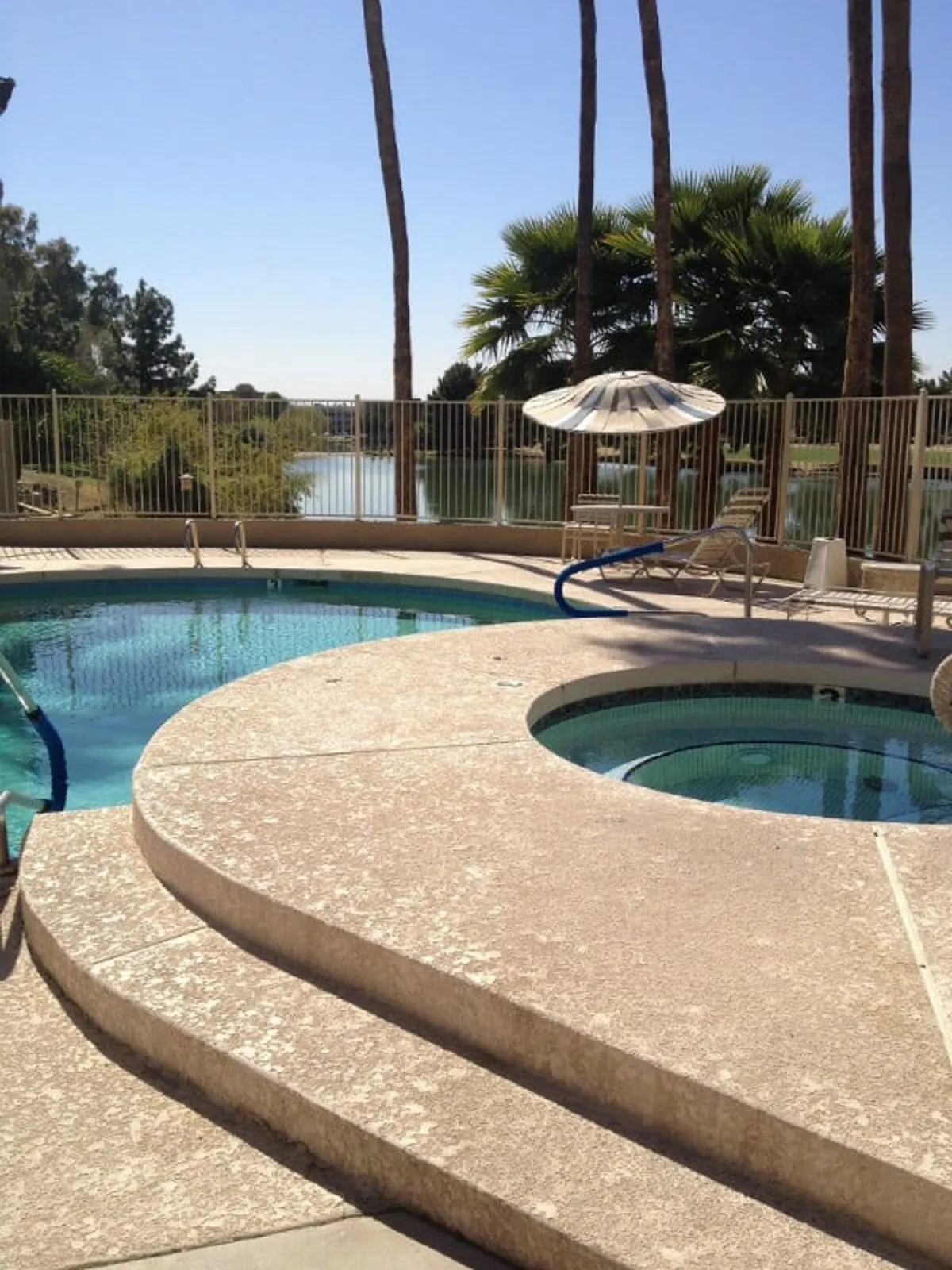 This image showcases a sparkling swimming pool and hot tub with palm trees and a scenic lake view in the background. Poolside lounge chairs invite relaxation, and the setting suggests a tranquil spot to unwind after a round of golf.