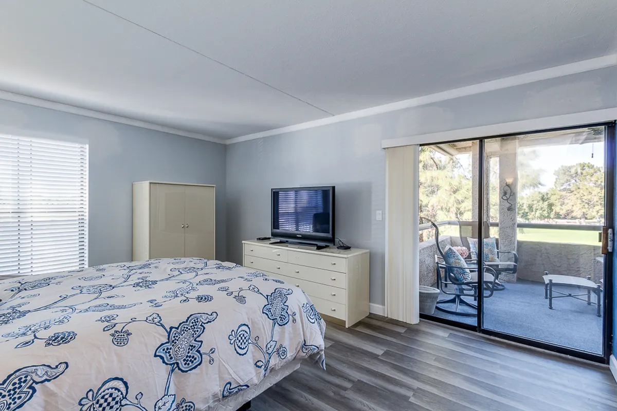 A tranquil bedroom with floral bedding and a sliding glass door leading to an outdoor seating area, inviting natural light and offering a seamless connection between indoor comfort and the balcony's outdoor oasis.