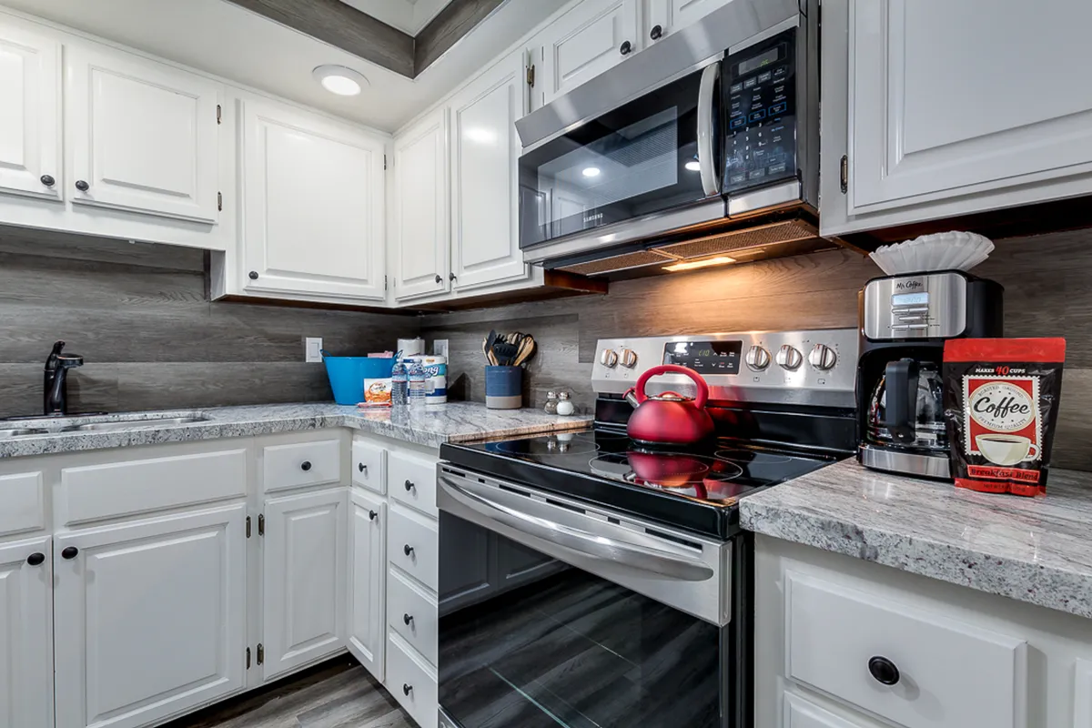 A closer view of the kitchen, focusing on stainless steel appliances, a granite countertop, a red kettle, and a coffee maker. The setup hints at morning routines and social cooking sessions, with an intimate, cozy mood.