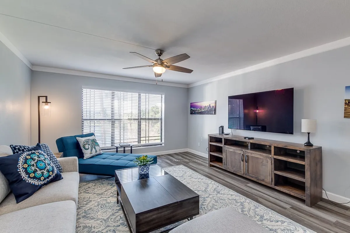 A cozy living room setup featuring a comfortable sofa with a throw blanket, a coffee table, TV, and a large window that brings in natural light. A lamp adds to the warm ambiance, and the layout is perfect for watching TV or enjoying peaceful downtime.